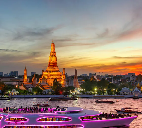 Wat Arun temple and illuminated cruise ship at twilight in Bangkok, Thailand.