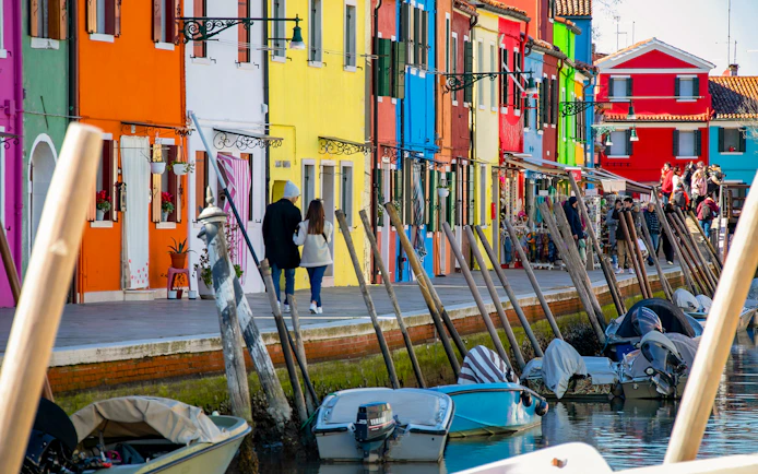 Colorful houses along Burano canal with boats, Venice afternoon tour from Punta Sabbioni.