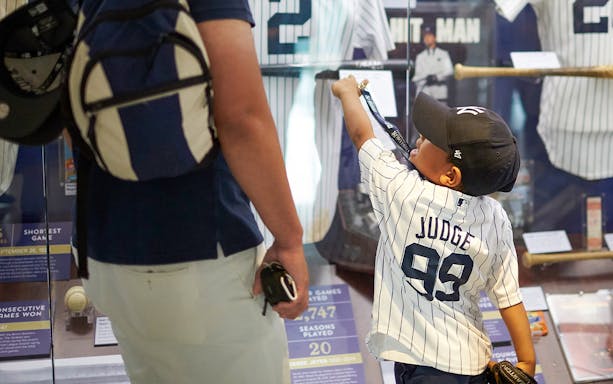 Child in Yankees jersey pointing at baseball exhibit in New York museum.