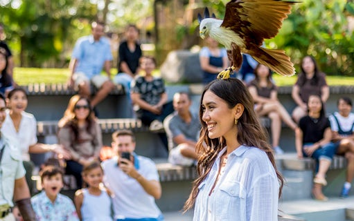 Woman smiling with a bird perched on her head at Bali Bird Park, audience in background.