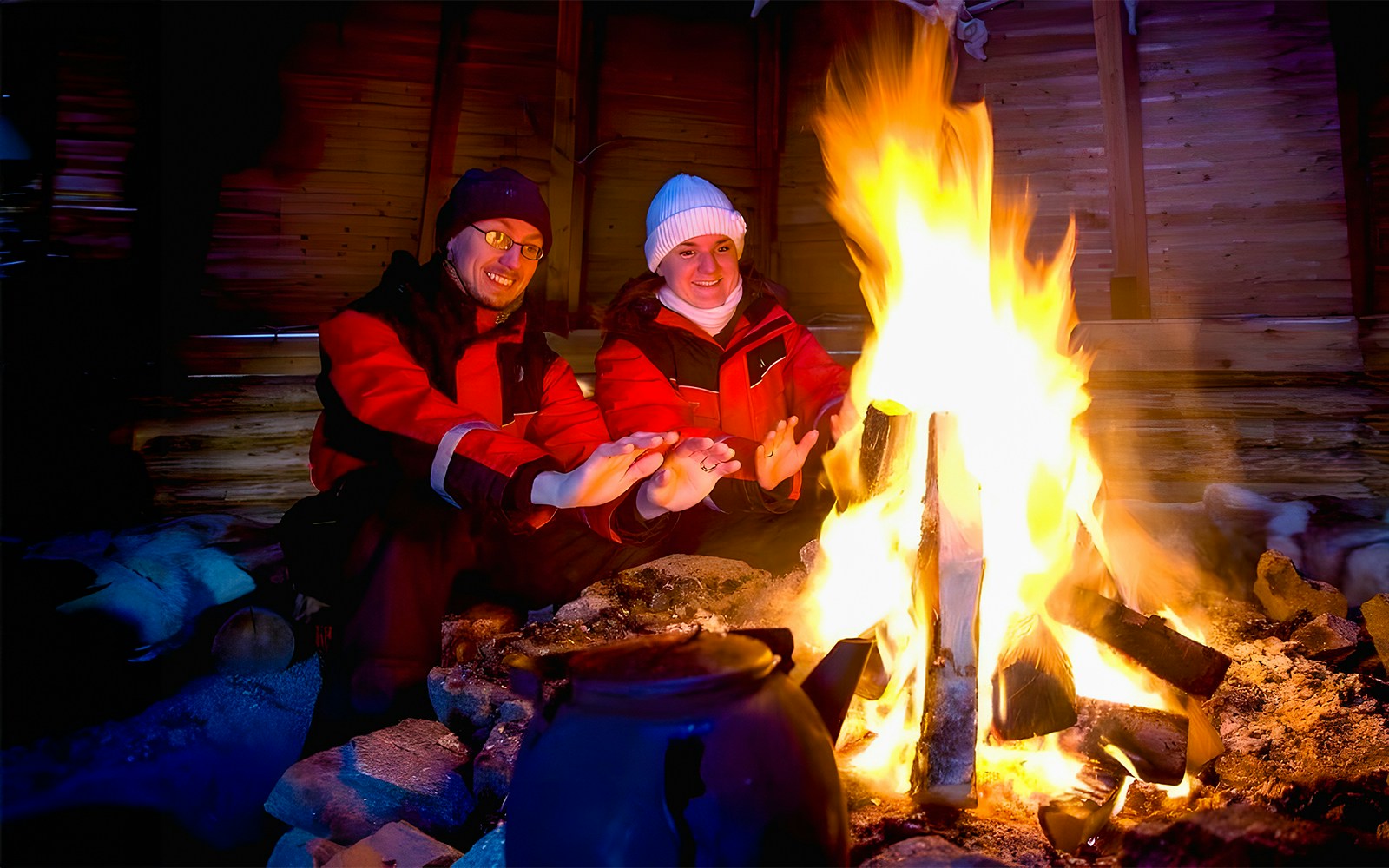 Tourists warming hands by a campfire in snowy Rovaniemi, Finland.