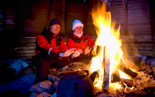 Tourists warming hands by a campfire in snowy Rovaniemi, Finland.