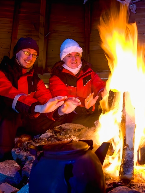 Tourists warming hands by a campfire in snowy Rovaniemi, Finland.