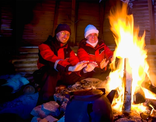 Tourists warming hands by a campfire in snowy Rovaniemi, Finland.