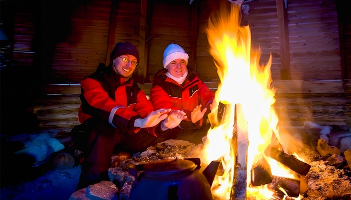 Tourists warming hands by a campfire in snowy Rovaniemi, Finland.