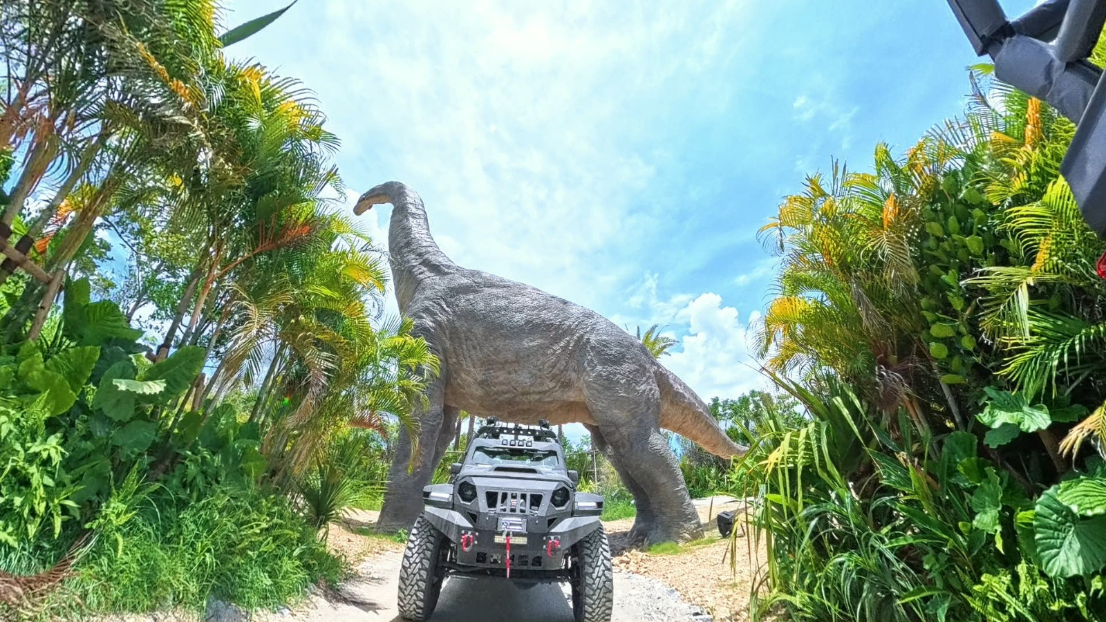 Off-road vehicle under dinosaur statue at JUNGLIA OKINAWA Park.