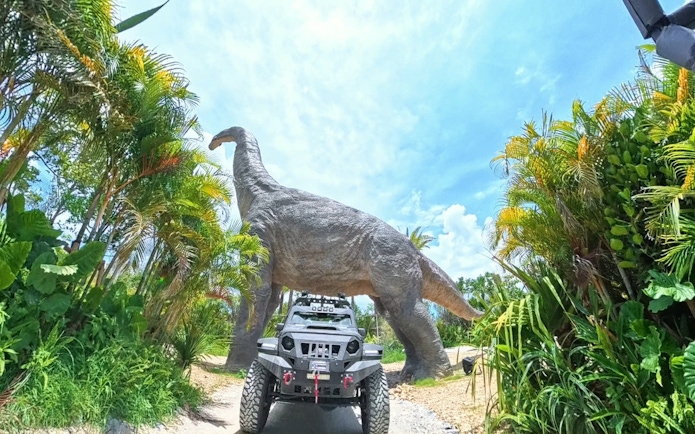 Off-road vehicle under dinosaur statue at JUNGLIA OKINAWA Park.