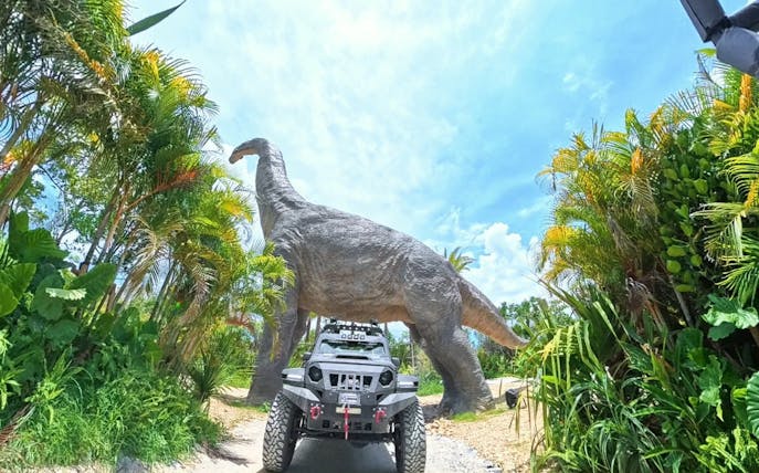 Off-road vehicle under dinosaur statue at JUNGLIA OKINAWA Park.