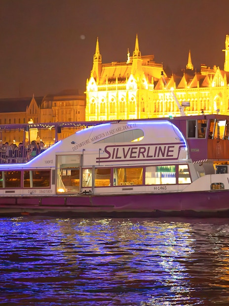 Cruise boat on the Danube in Budapest at night, near illuminated Parliament building.