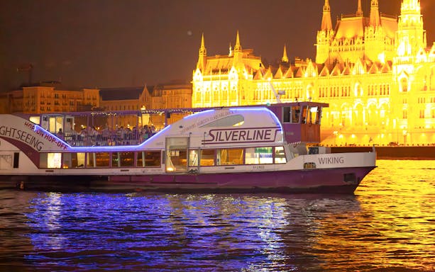 Cruise boat on the Danube in Budapest at night, near illuminated Parliament building.