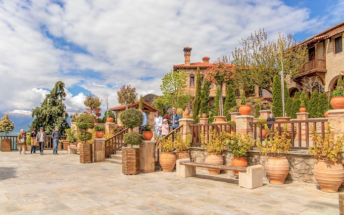 Guests exploring a courtyard in a Meteora monastery, surrounded by potted plants and historic architecture.