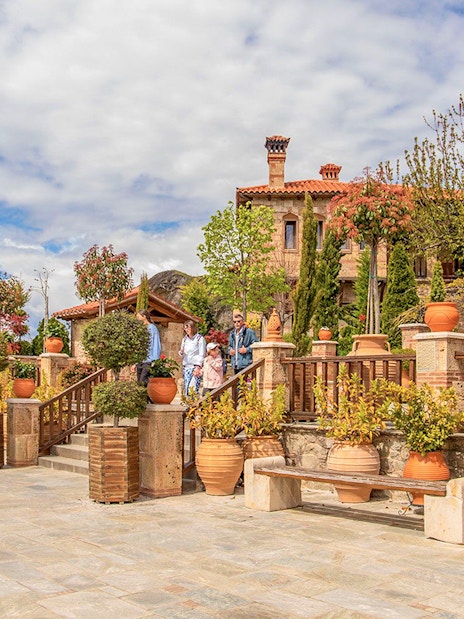 Guests exploring a courtyard in a Meteora monastery, surrounded by potted plants and historic architecture.