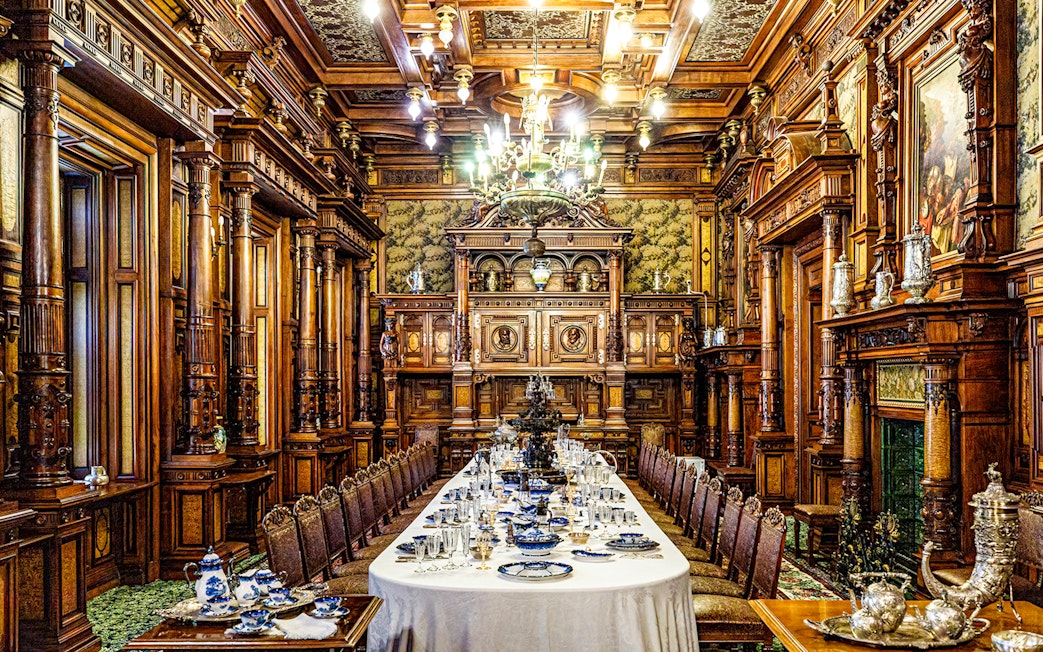 Elegant dining room inside Peles Castle with ornate woodwork and a long table set for a banquet.