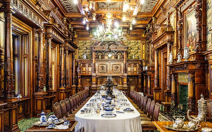 Elegant dining room inside Peles Castle with ornate woodwork and a long table set for a banquet.