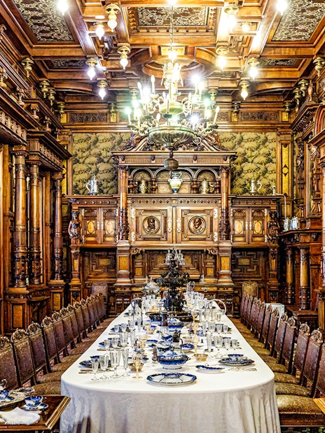 Elegant dining room inside Peles Castle with ornate woodwork and a long table set for a banquet.