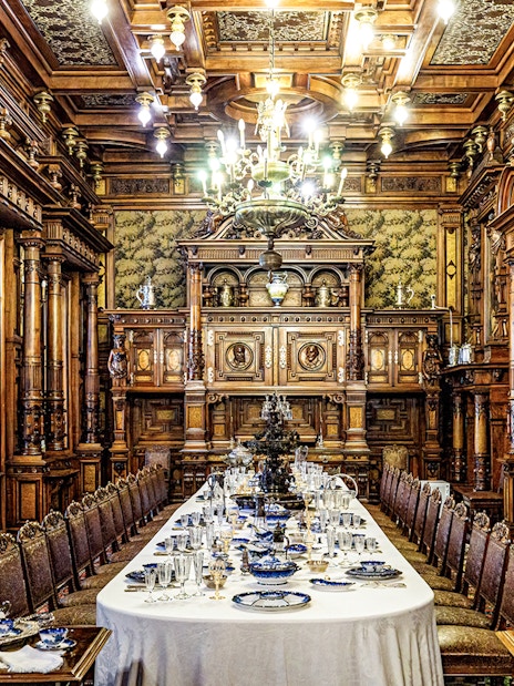Elegant dining room inside Peles Castle with ornate woodwork and a long table set for a banquet.
