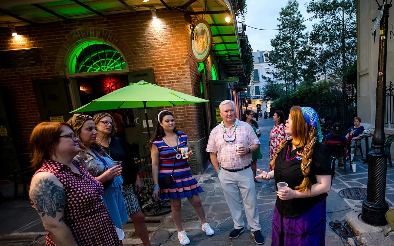 Group on New Orleans craft cocktail walking tour outside a bar with green umbrella.
