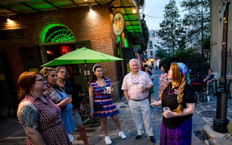 Group on New Orleans craft cocktail walking tour outside a bar with green umbrella.