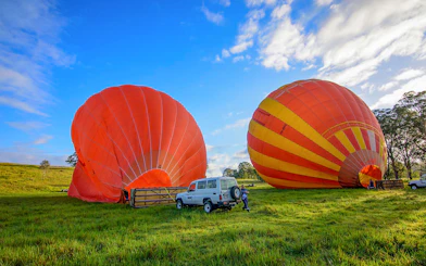Hot air balloons inflating on a grassy field in Cairns, Australia, with a vehicle nearby.