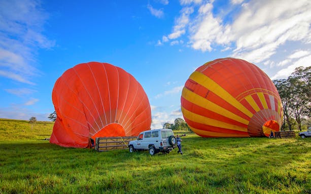 Hot air balloons inflating on a grassy field in Cairns, Australia, with a vehicle nearby.