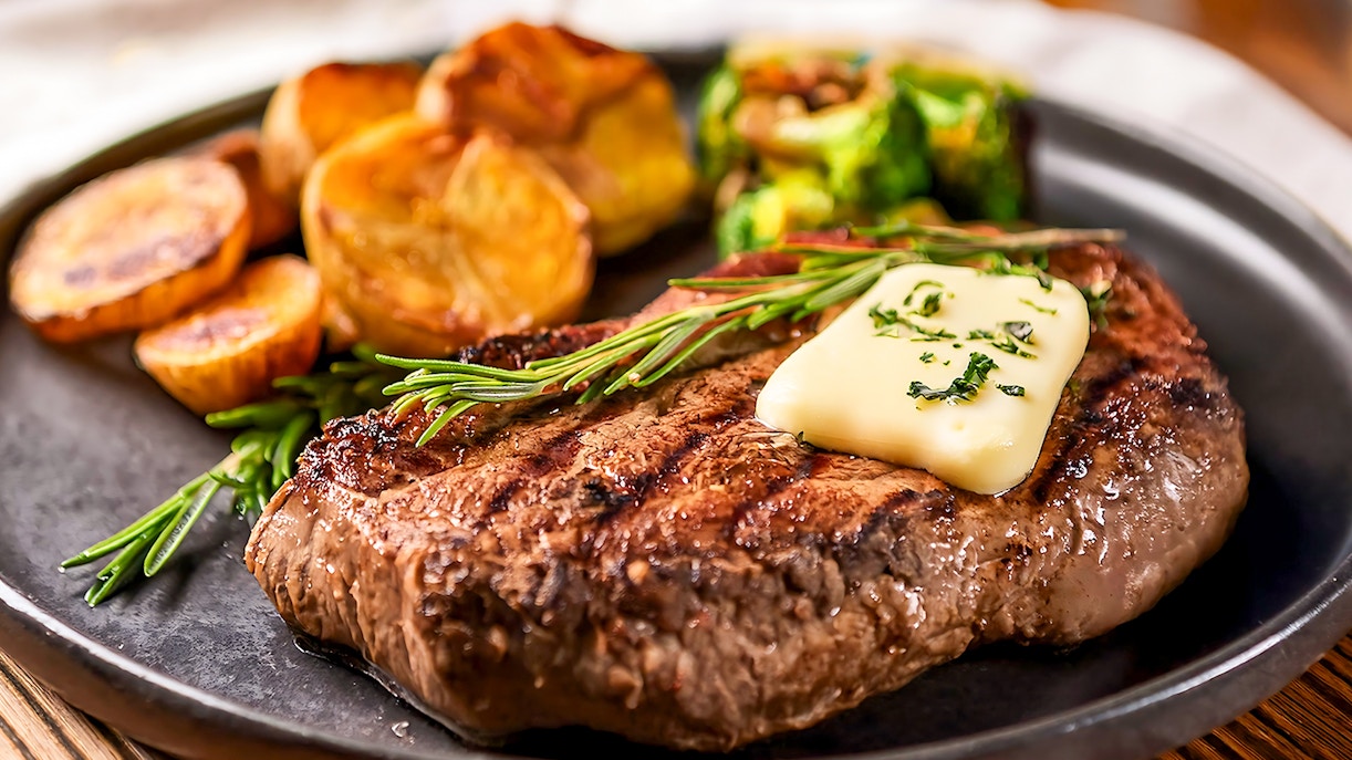 Buttered steak with herbs and potatoes on a plate.