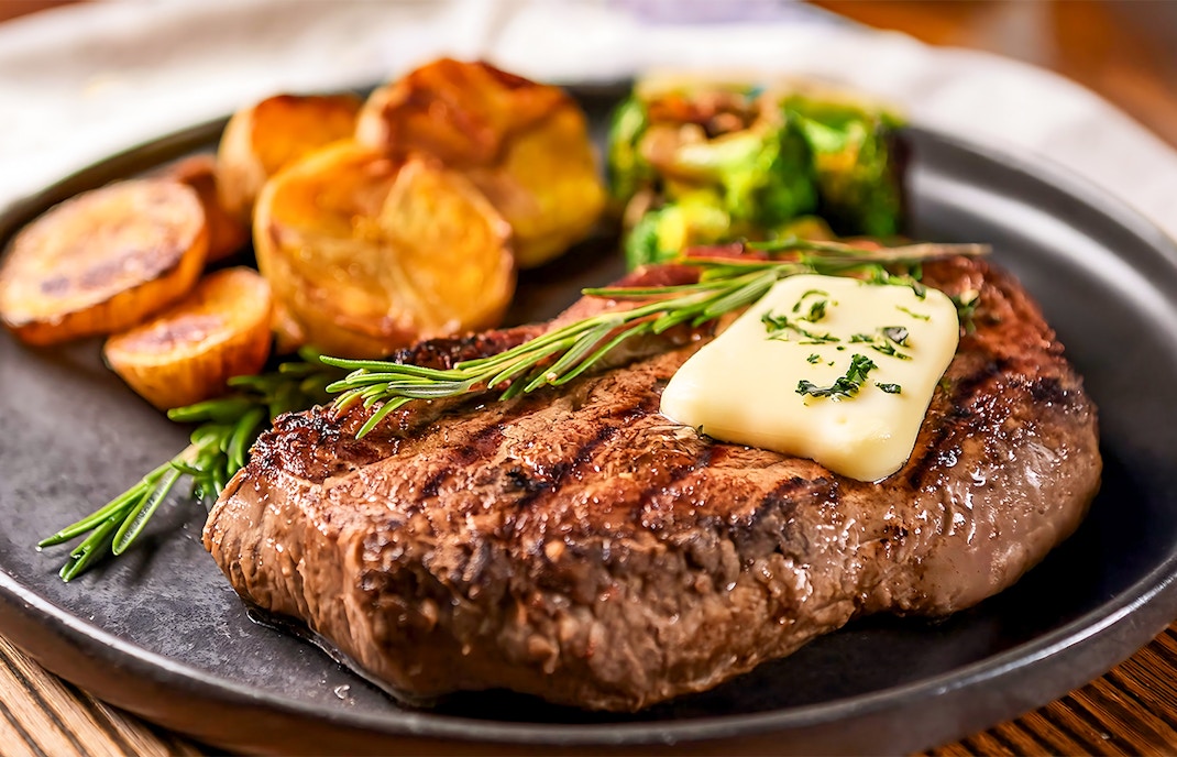 Buttered steak with herbs and potatoes on a plate.