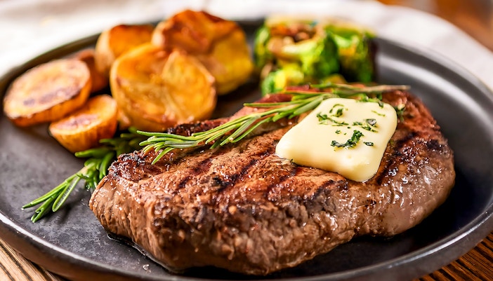 Buttered steak with herbs and potatoes on a plate.
