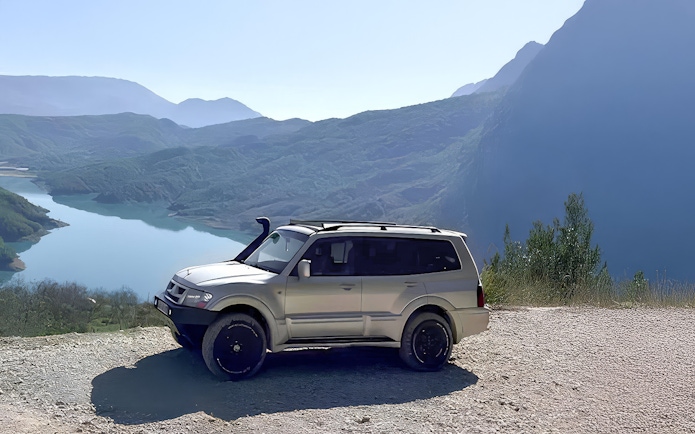 4x4 vehicle parked with Bovilla Lake and mountains in the background during offroad tour from Tirana.