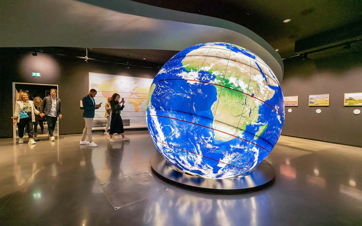 Visitors exploring a large illuminated globe at The Wine Experience exhibit.