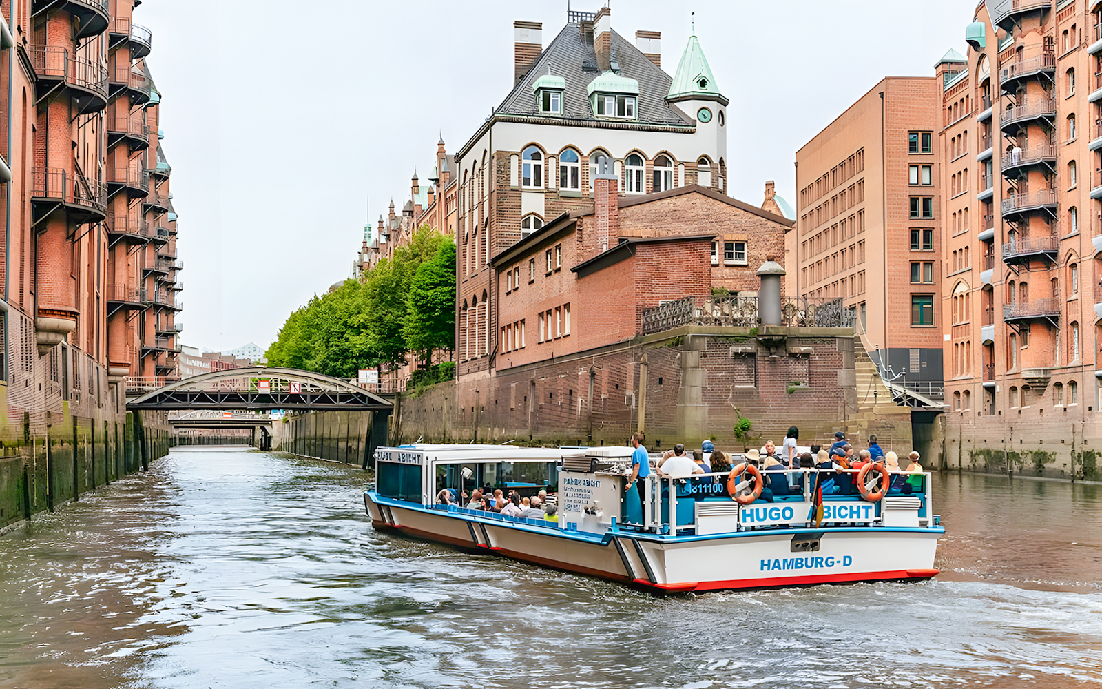 Harbor cruise boat navigating through Hamburg's Speicherstadt district canal.