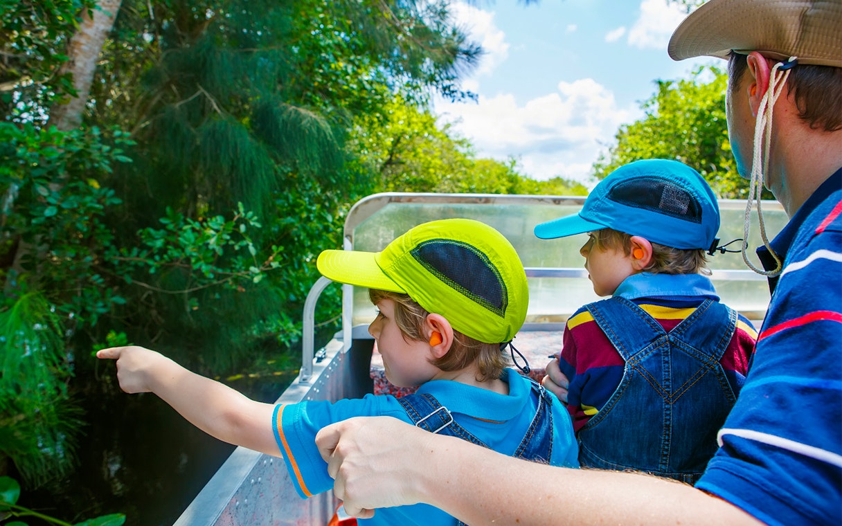 Children on an airboat tour in the Everglades, Miami, pointing at wildlife.