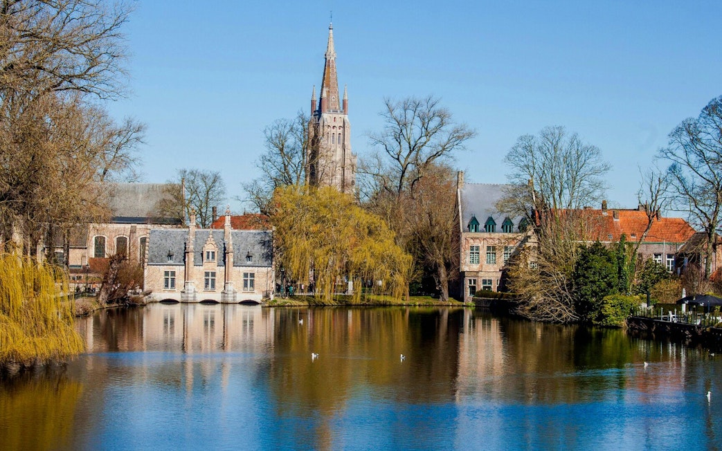 Minnewater Lake in Bruges, Belgium, with historic buildings and trees reflected in the water.