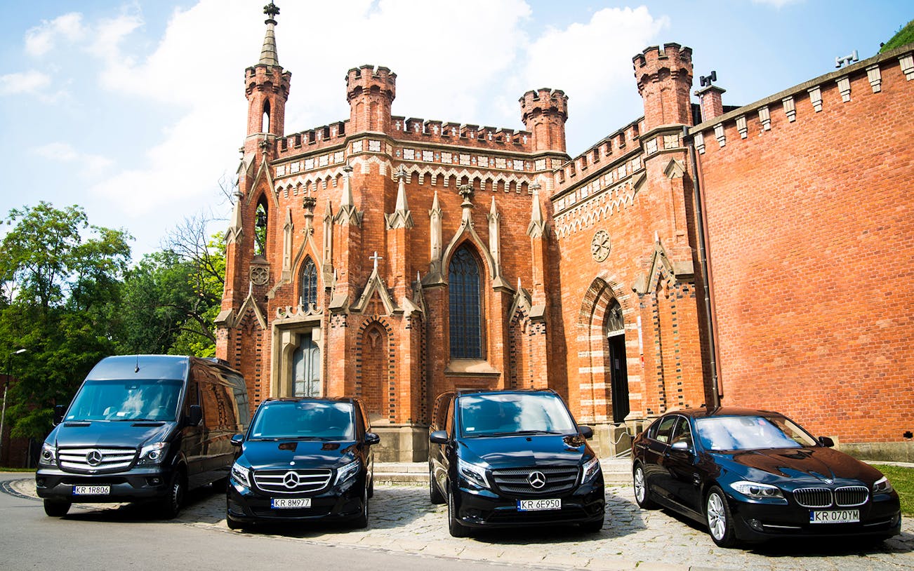 Transfer vehicles parked in front of a historic brick building in Krakow.