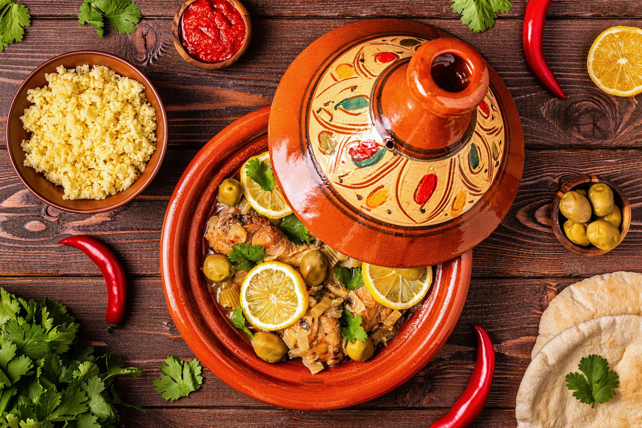 Moroccan tagine with chicken, olives, and lemon slices served with couscous and bread.