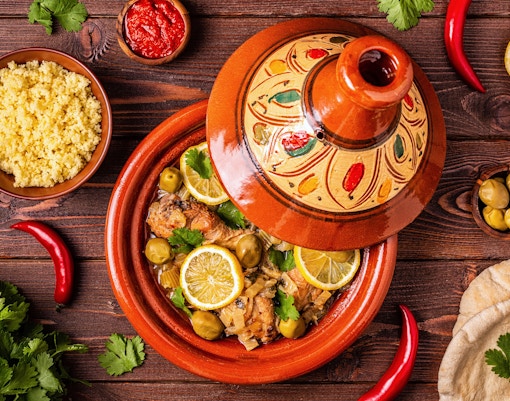 Moroccan tagine with chicken, olives, and lemon slices served with couscous and bread.