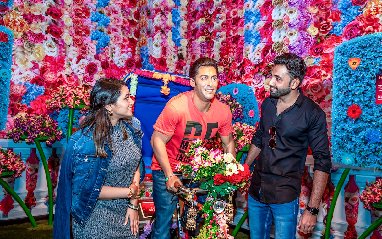 Visitors interacting with a wax figure at Dubai Madame Tussauds, surrounded by colorful flowers.
