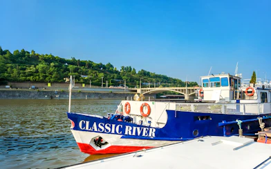 River cruise boat docked near a bridge, ready for an evening dinner cruise with live music.