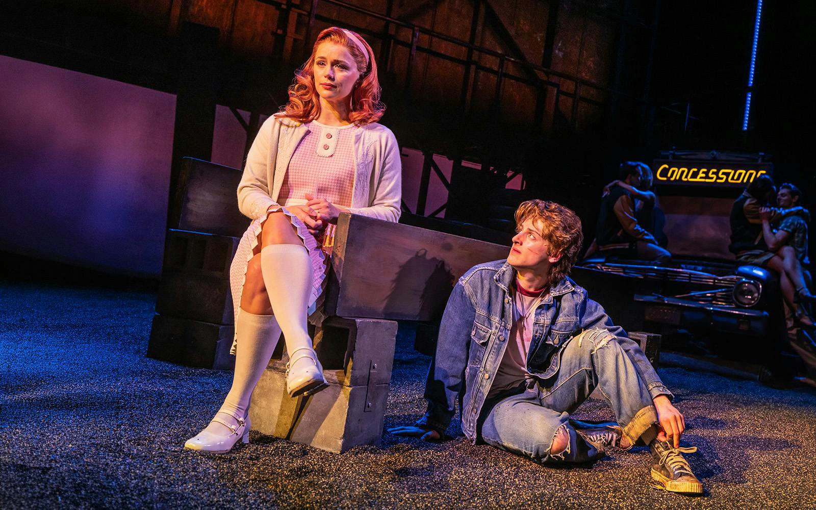 Stage scene from The Outsiders on Broadway with two characters seated, one on a bench and one on the ground.