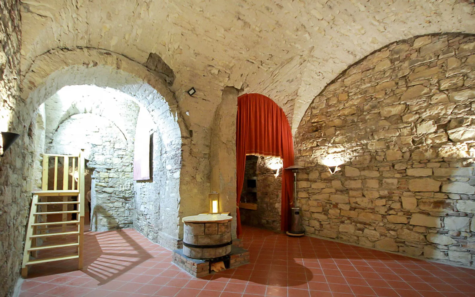 Inside stone-walled chamber of Minorite monastery of St James, Prague, with arched ceilings and red curtain.