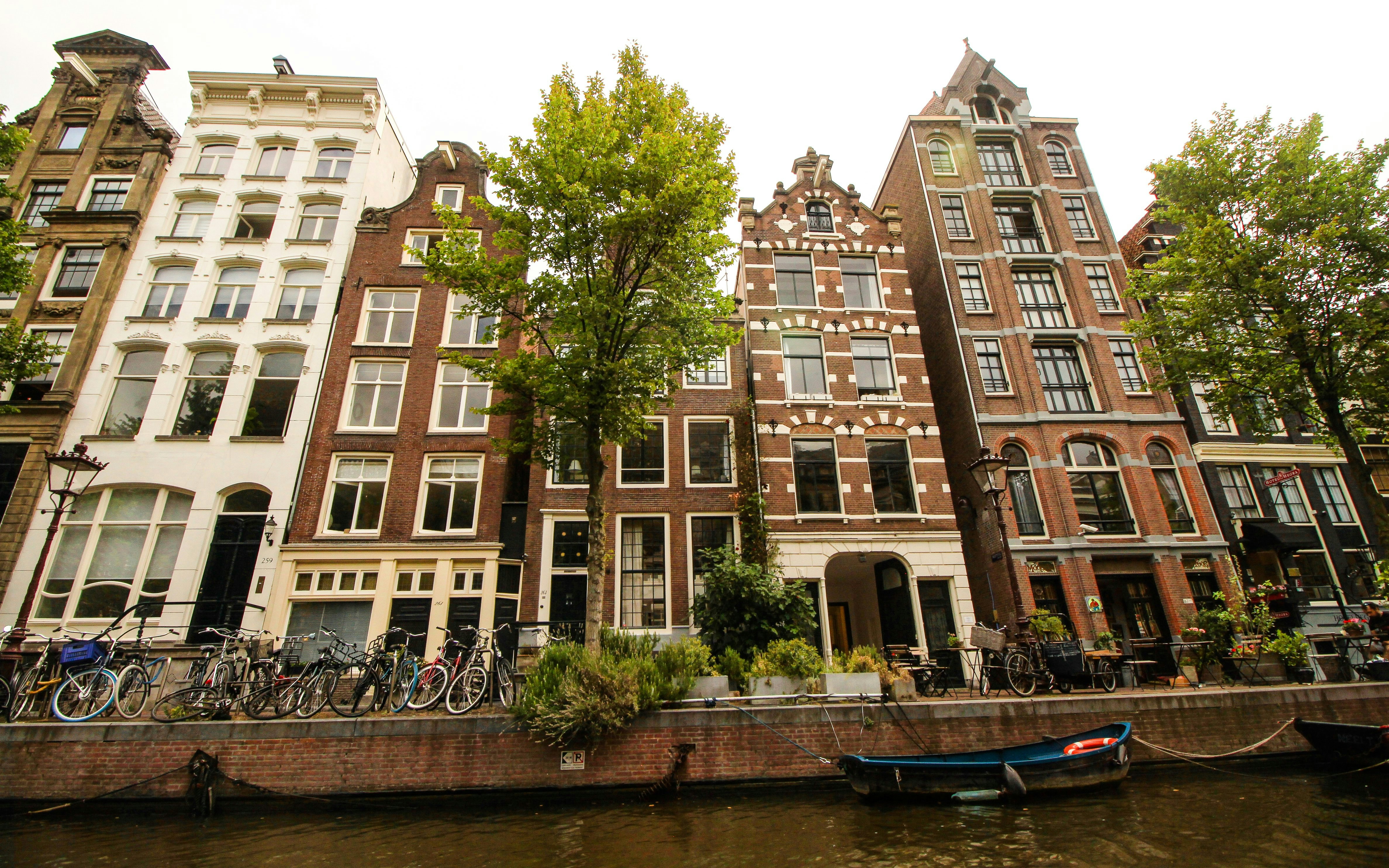 Narrow canal-side houses in Amsterdam with bicycles and trees.