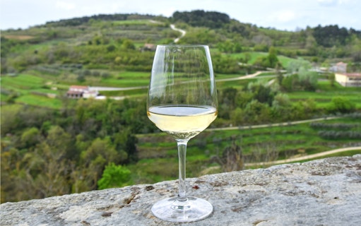 White wine glass on stone ledge overlooking green hills and roads in Croatian countryside.