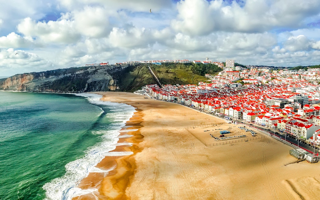 Panoramic view of Nazaré beach and town, Portugal, with cliffs and ocean waves.
