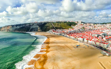 Panoramic view of Nazaré beach and town, Portugal, with cliffs and ocean waves.