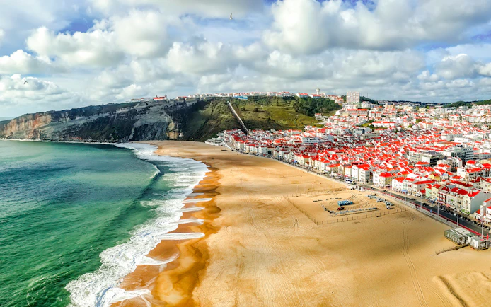 Panoramic view of Nazaré beach and town, Portugal, with cliffs and ocean waves.