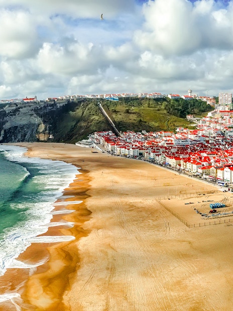 Panoramic view of Nazaré beach and town, Portugal, with cliffs and ocean waves.
