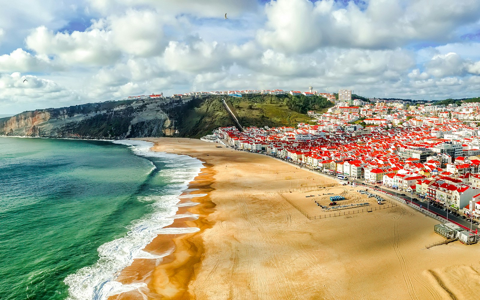 Panoramic view of Nazaré beach and town, Portugal, with cliffs and ocean waves.