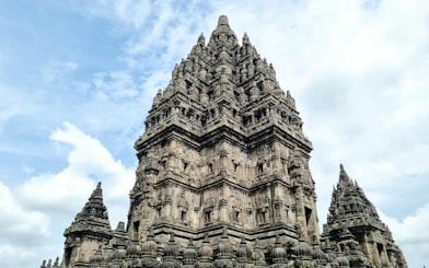 Prambanan Temple's central tower with intricate stone carvings against a cloudy sky.