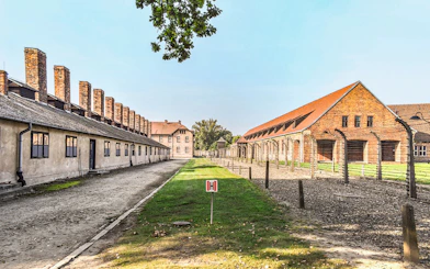 Auschwitz I barracks with barbed wire fences and brick buildings under a clear sky.