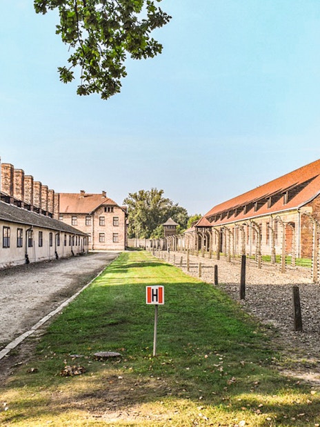 Auschwitz I barracks with barbed wire fences and brick buildings under a clear sky.
