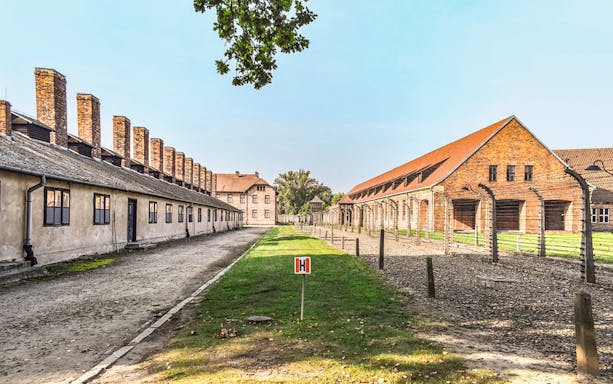 Auschwitz I barracks with barbed wire fences and brick buildings under a clear sky.